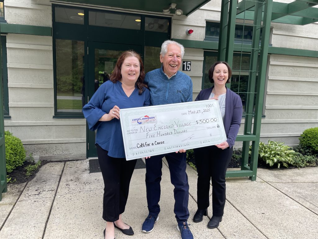 Cotti Johnson representatives presenting a $500 donation check to New England Village, highlighting community support for individuals with intellectual and developmental disabilities.